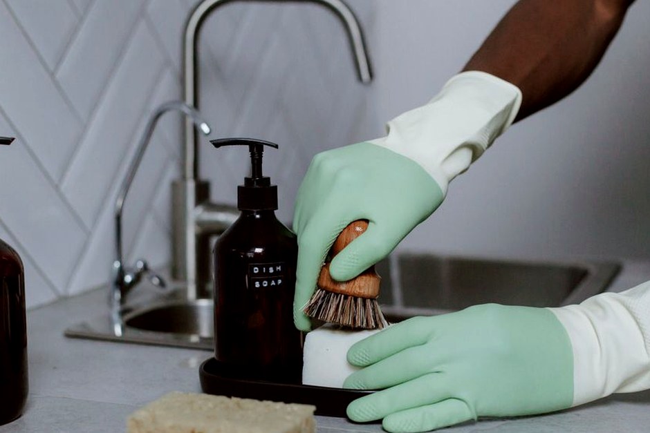 Hands in latex gloves washing dishes with soap at a kitchen sink.