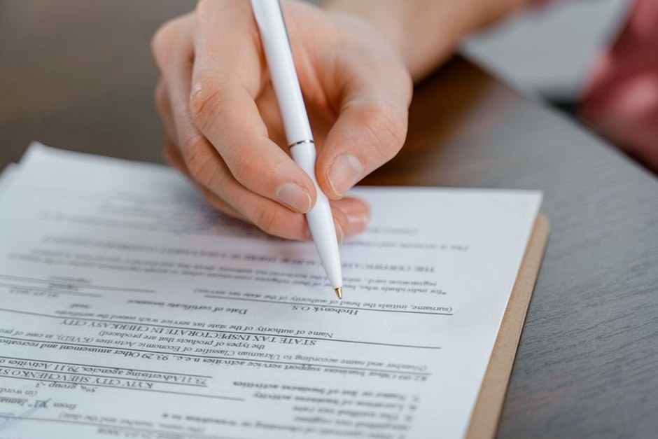 A hand holding a pen signing a document, close-up shot with focus on the paper.