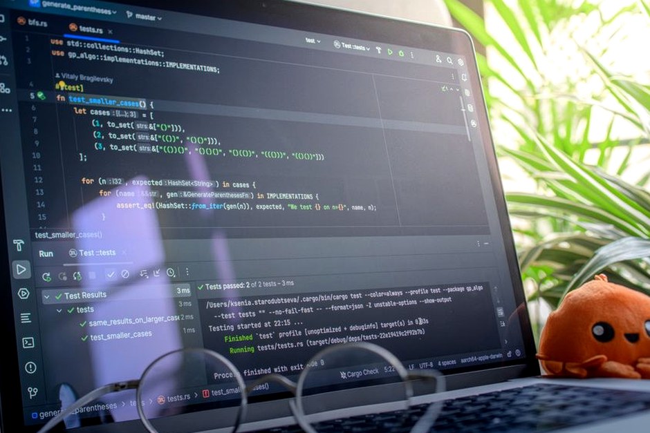Open laptop displaying code next to a plush toy, set in a bright room with plants.